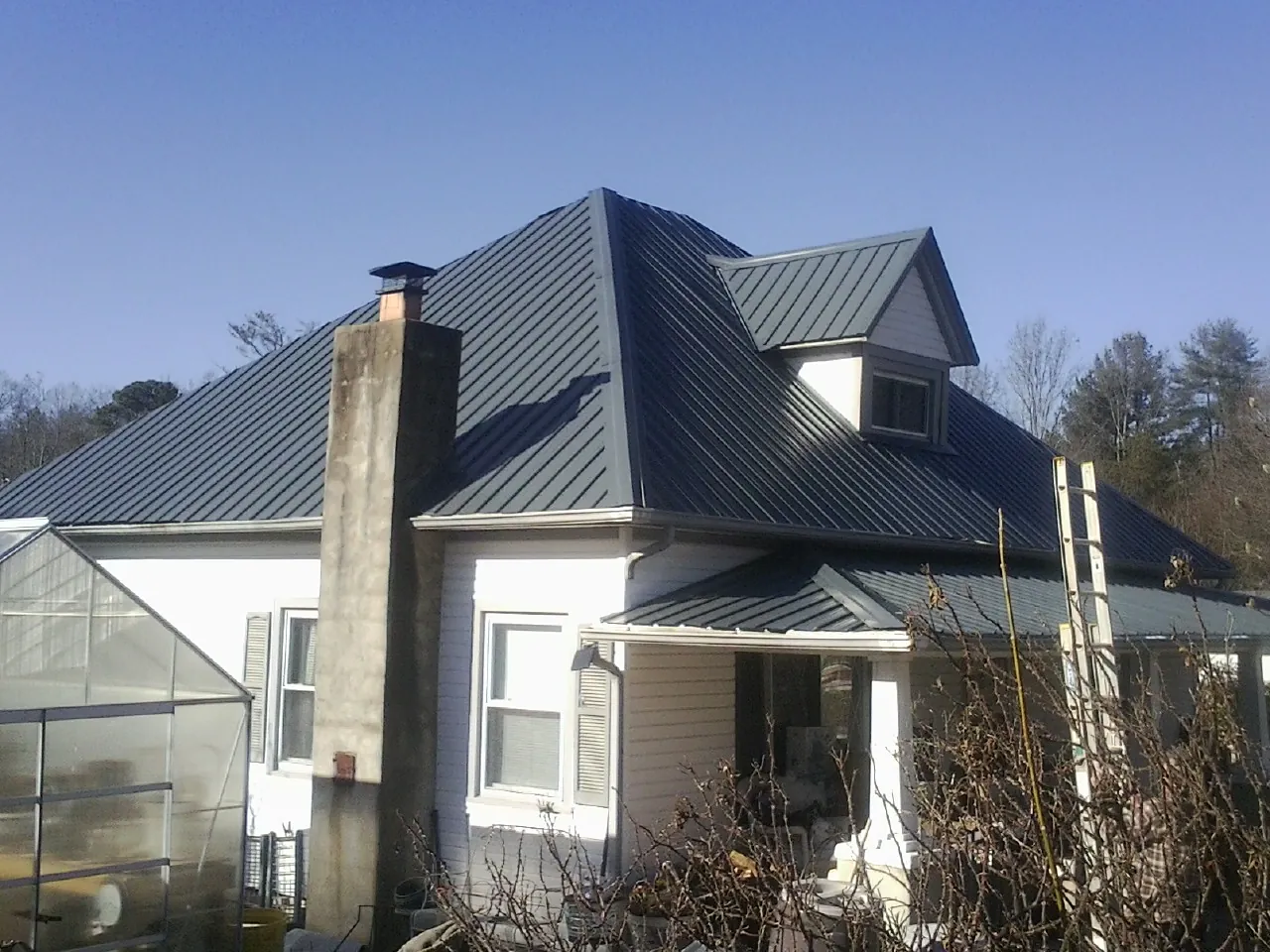 Dark blue standing seam metal roof on a white farmhouse with dormer — Slate & Tile Roof Repair by Roofing Brothers in Wisconsin Dells