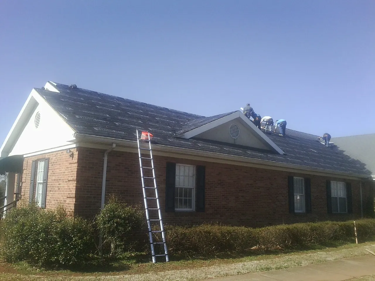 Crew tearing shingles off a brick ranch roof with a ladder set — Metal Roof Repair work by our crew in Wisconsin Dells