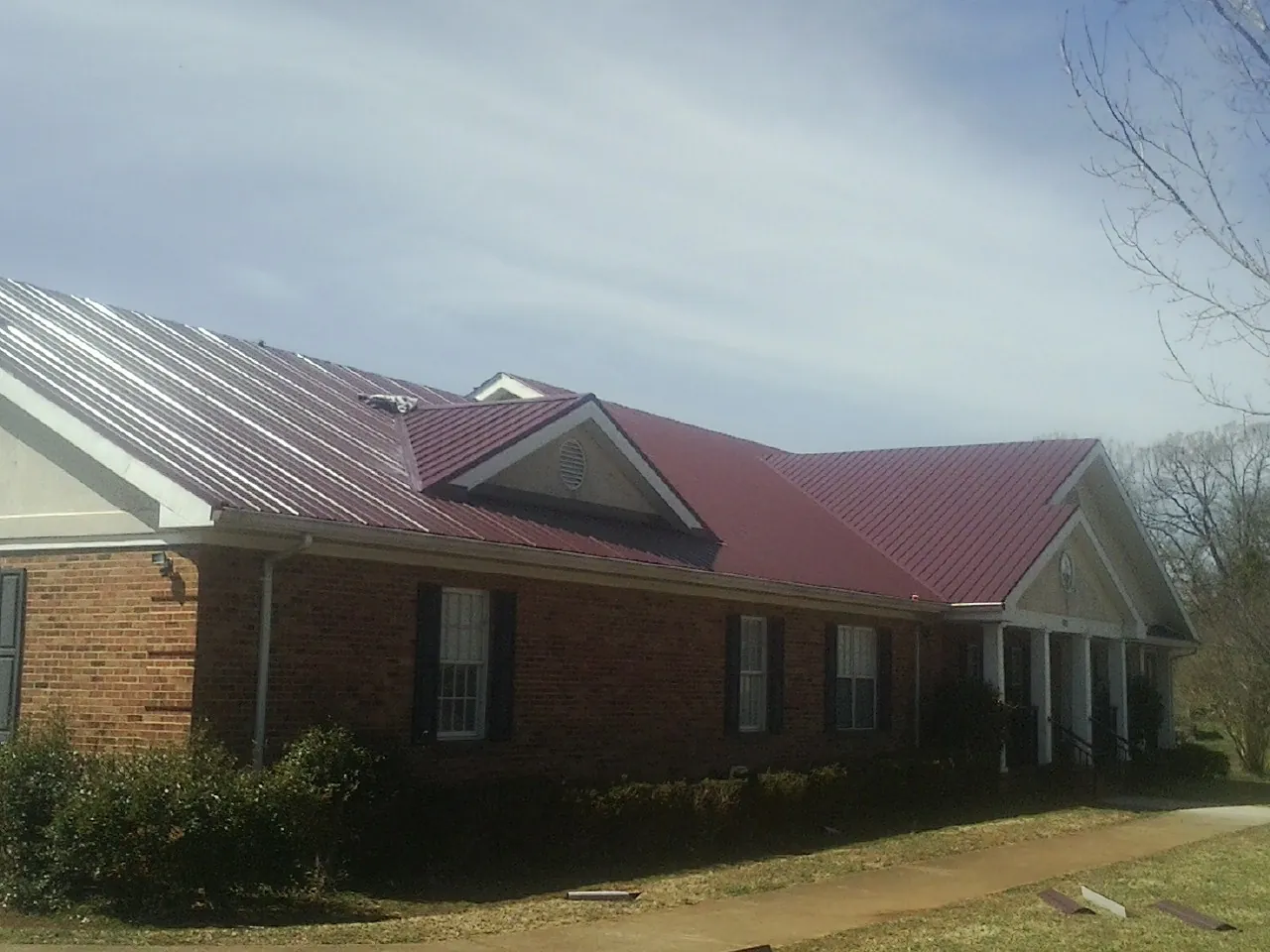 Red metal roof with gabled entries on a long brick building, from a Hail Damage Roof Repair job in Wisconsin Dells