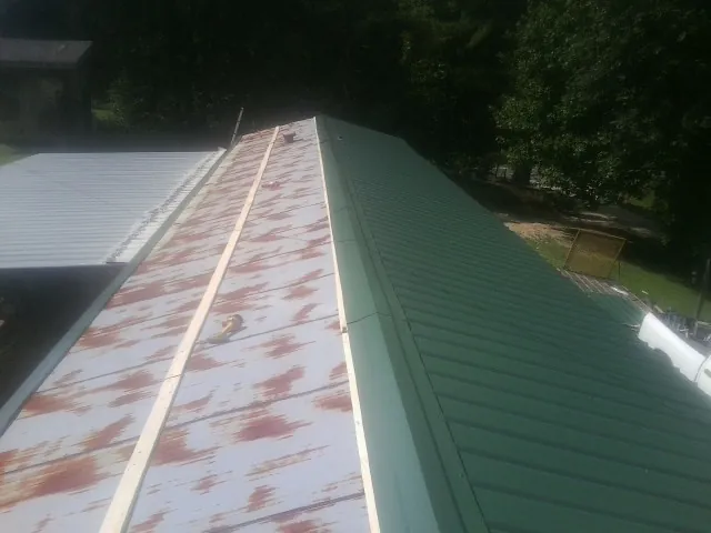 Old rusted panels beside newly installed green metal roofing — Wind Damage Roof Repair by Roofing Brothers in Wisconsin Dells