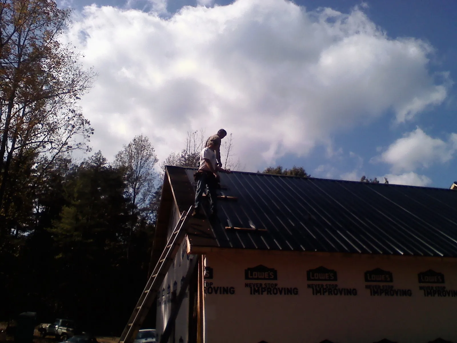 Roofer fastening dark metal panels high against a cloudy sky, from a Roof Inspection job in Wisconsin Dells