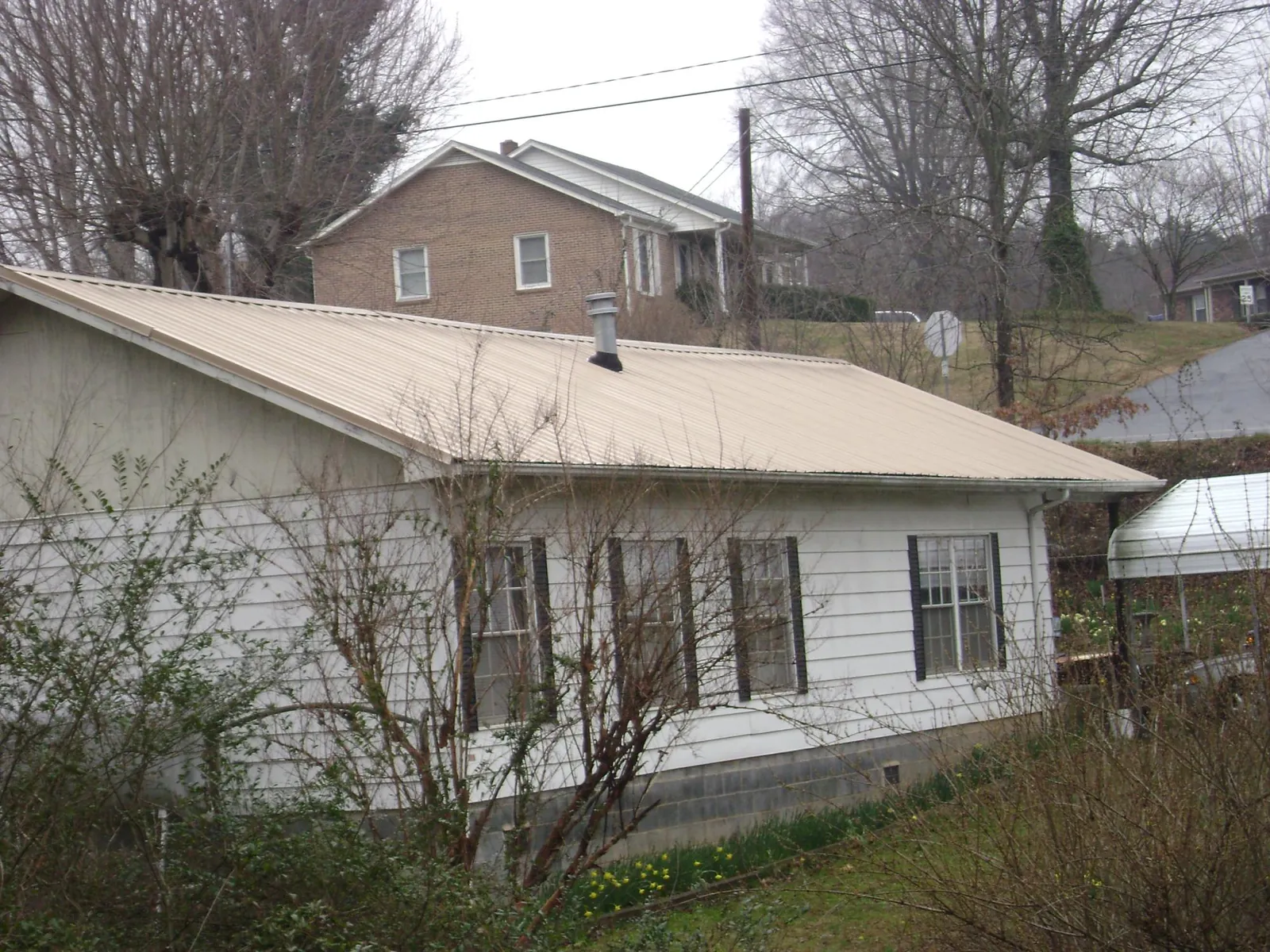 Tan metal roof on a white sided house set into a hillside — Commercial Roofing by Roofing Brothers in Wisconsin Dells